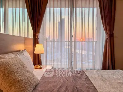 Cozy bedroom with stunning city view at sunset, featuring elegant curtains and warm lighting.