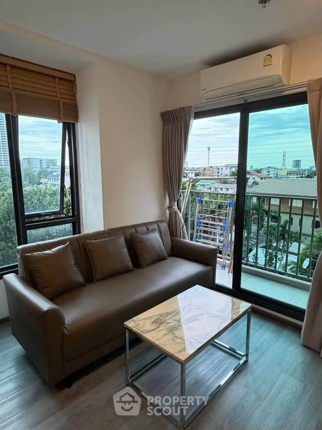 Modern living room with large windows and city view, featuring a stylish sofa and marble coffee table.