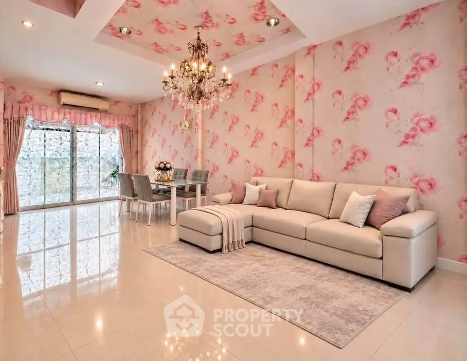 Elegant living room with floral wallpaper and chandelier, featuring a spacious sofa and dining area.
