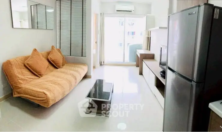 Modern living room with cozy sofa, sleek coffee table, and stainless steel fridge in bright apartment.