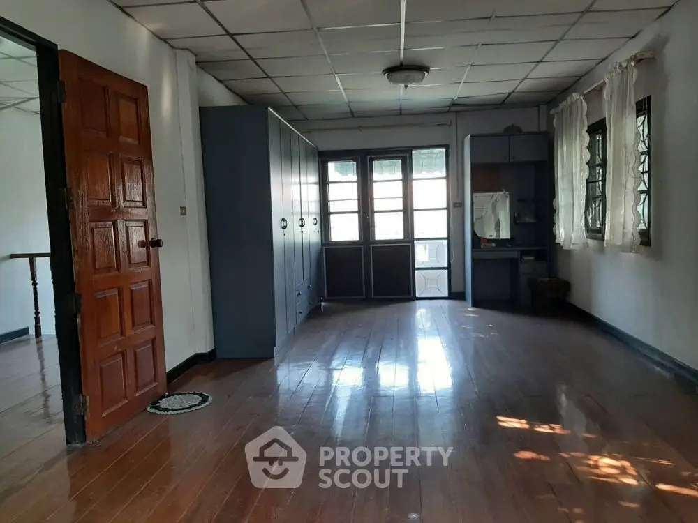 Spacious room with wooden flooring and ample natural light, featuring built-in storage and classic wooden door.