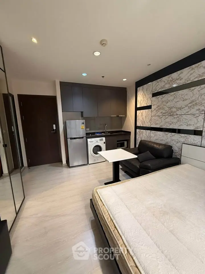 Modern studio apartment with sleek kitchen and cozy living area, featuring a washing machine and stylish decor.