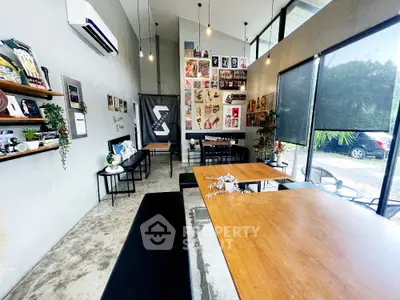 Modern industrial-style room with high ceilings and large windows, perfect for creative workspace or cafe.