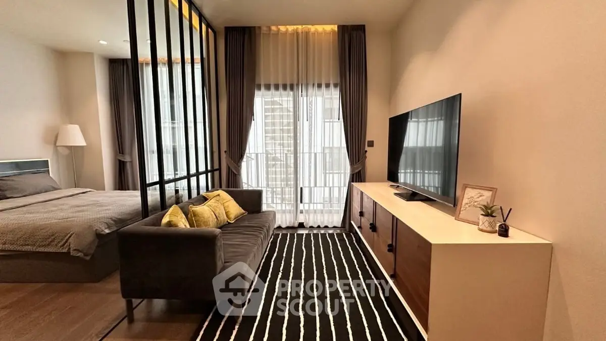 Modern living room with stylish decor and large TV, adjacent to a cozy bedroom.