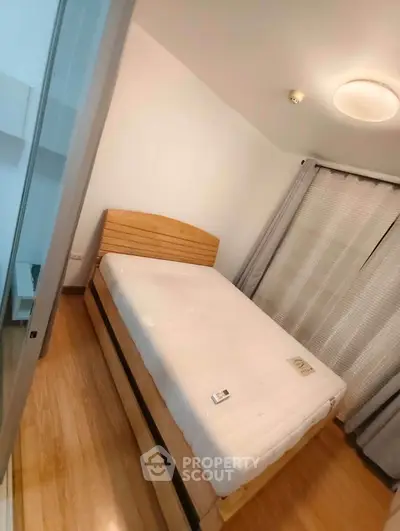 Cozy bedroom with wooden flooring and natural light, featuring a comfortable bed and modern decor.