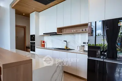 Modern kitchen with sleek white cabinets and marble countertops, featuring a black fridge and built-in oven.