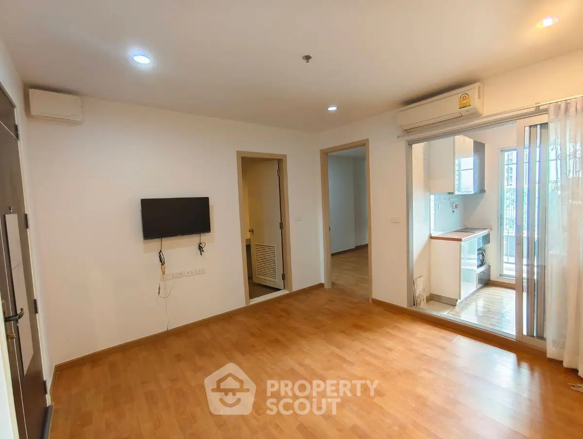 Spacious empty living room with wooden flooring and modern kitchen view.