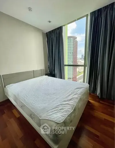 Spacious bedroom with large window offering stunning city views and elegant wooden flooring.