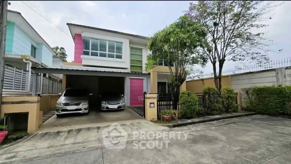 Modern two-story house with carport and lush greenery in a suburban neighborhood.