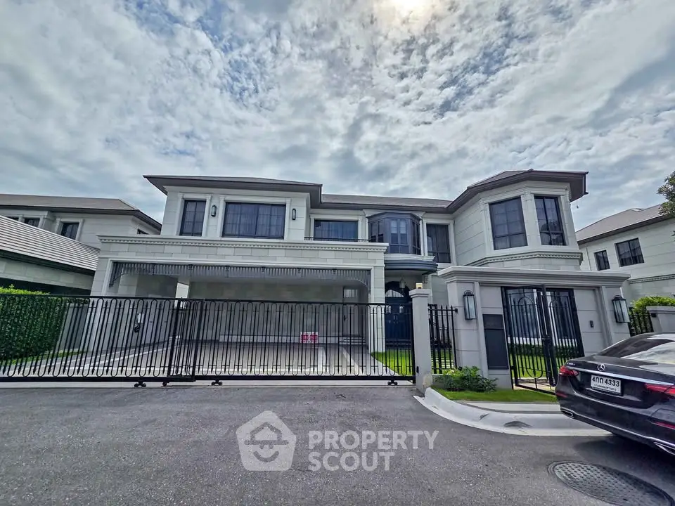 Luxurious modern mansion with gated entrance and elegant facade under a cloudy sky.
