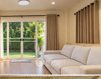 Spacious living room with large windows overlooking a lush garden, featuring a comfortable beige sofa.