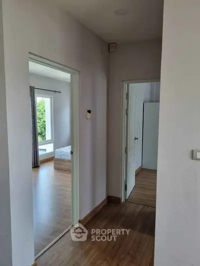 Bright hallway leading to a cozy bedroom with wooden flooring and large window.