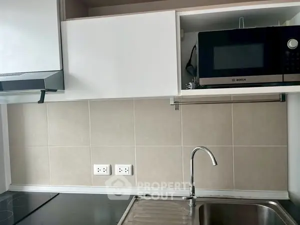 Modern kitchen with sleek cabinets, built-in microwave, and stainless steel sink.