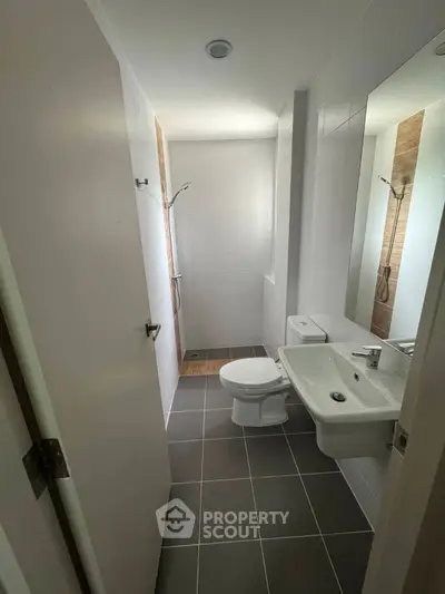 Modern bathroom with sleek fixtures and neutral tiles, featuring a shower and toilet.