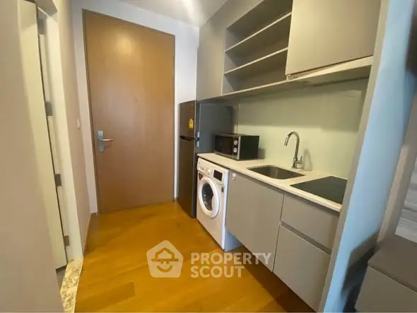 Modern compact kitchen with washing machine and microwave in sleek apartment.