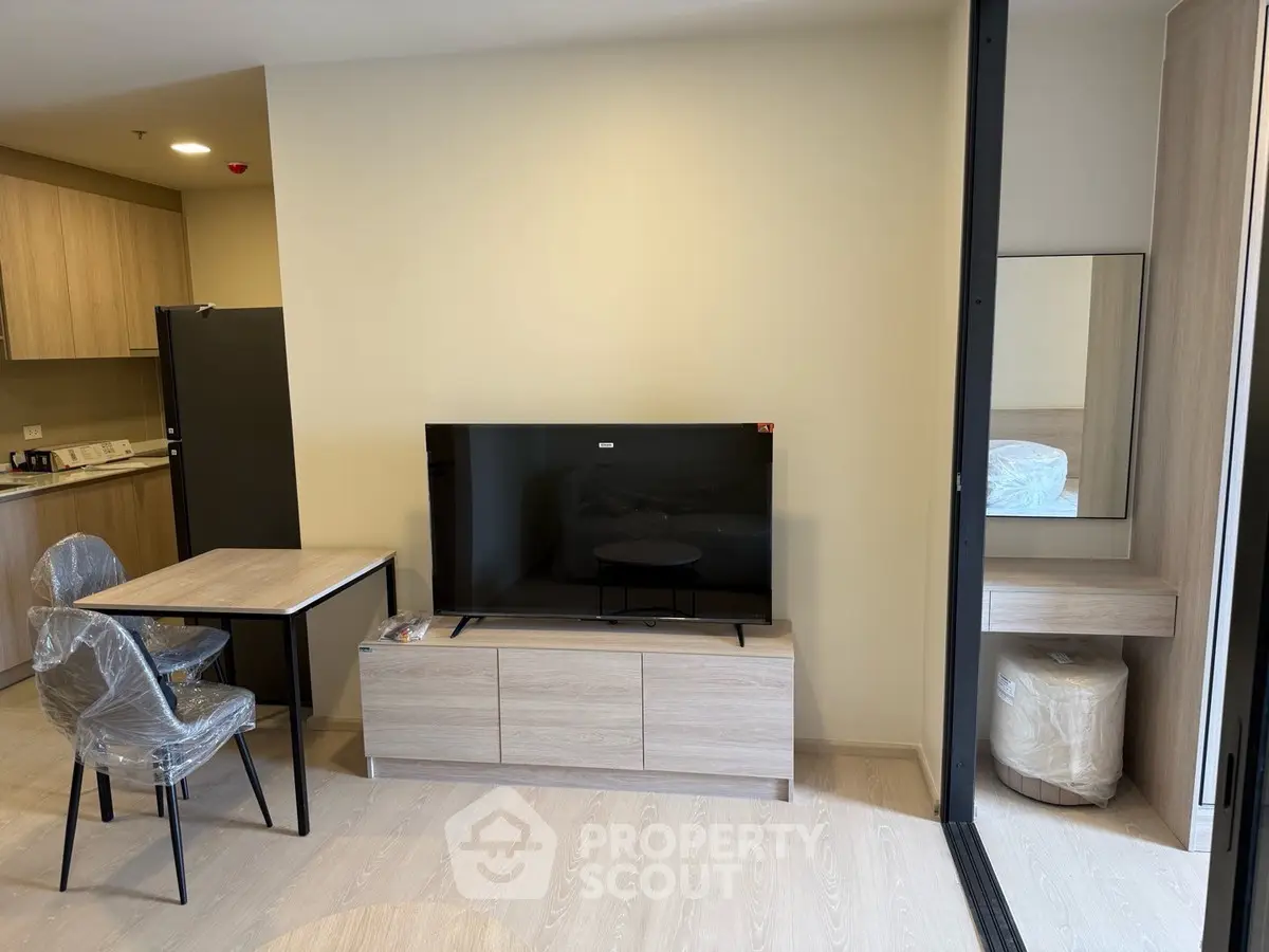 Modern living room with sleek TV setup and compact dining area in stylish apartment.