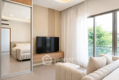 Modern living room with large TV, cozy sofa, and natural light from balcony.