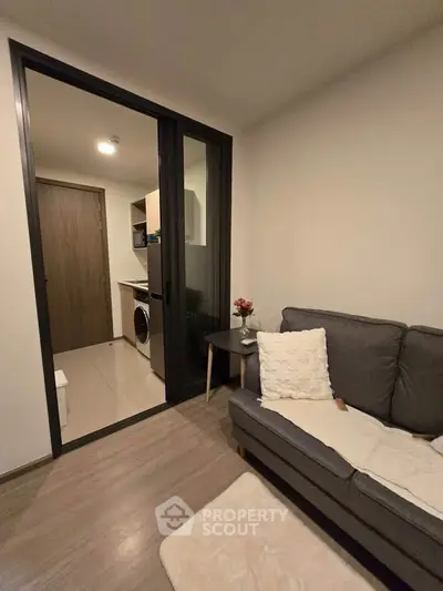 Modern living room with cozy sofa and view into compact kitchen with washing machine.