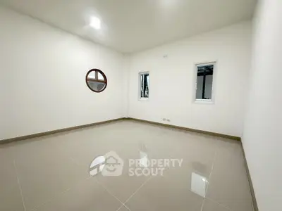 Spacious empty room with glossy tiled floor and unique round window design.