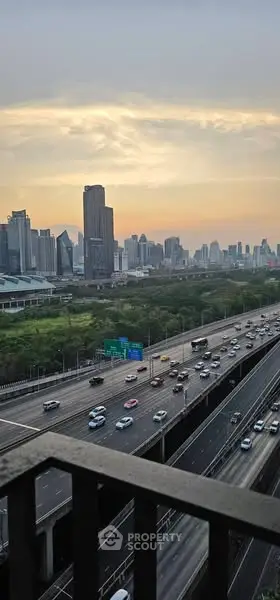 Stunning cityscape view from a high-rise balcony overlooking a bustling highway at sunset.