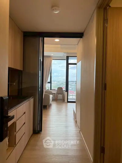 Modern apartment hallway leading to a bright living room with city view.