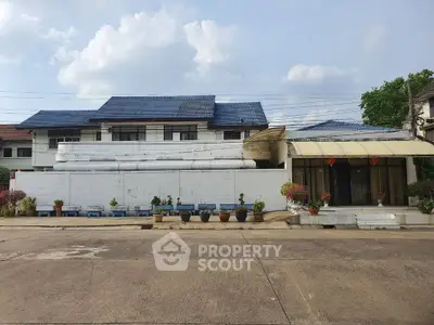Charming suburban house with blue roof and spacious driveway, surrounded by potted plants and greenery.