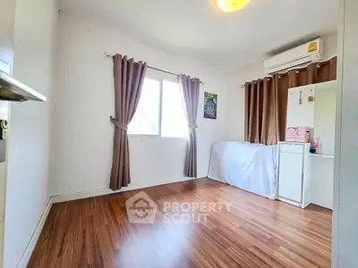 Spacious bedroom with wooden flooring and natural light, featuring air conditioning and elegant curtains.