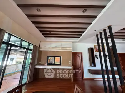 Spacious modern living room with wooden flooring and ceiling beams, featuring large windows for natural light.