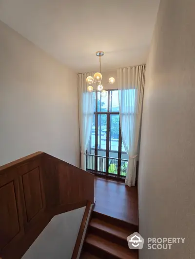 Elegant staircase with large window and modern chandelier in luxury home