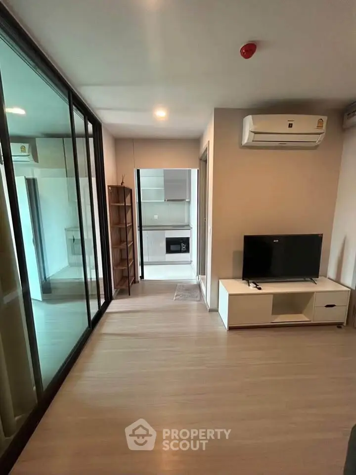 Modern living room with sleek design, featuring glass doors and compact kitchen area.