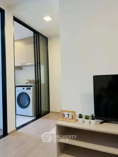 Modern living room with TV and view into laundry area with washing machine