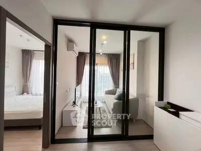 Modern apartment with glass partition separating living room and bedroom, featuring sleek decor and natural light.