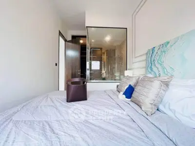 Modern bedroom with glass wall view into bathroom, featuring stylish decor and cozy bedding.