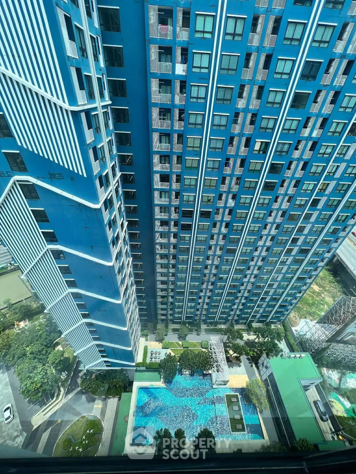 Stunning aerial view of modern high-rise building with luxurious pool area and lush greenery.