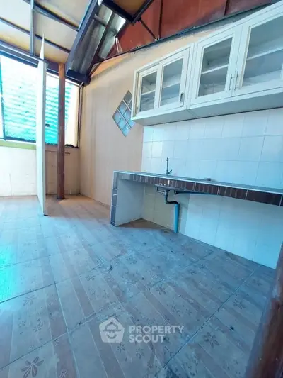 Spacious kitchen with tiled flooring and ample natural light, featuring a sleek countertop and upper cabinets.