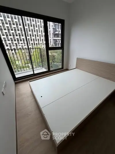 Modern bedroom with large window and minimalist bed frame, offering a serene view.