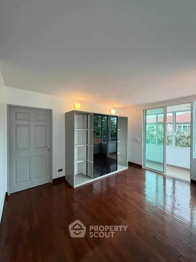 Spacious living room with glossy wooden floors and large windows opening to a balcony with a view.