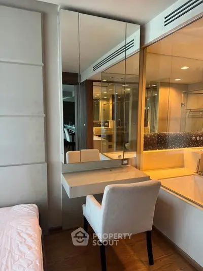 Modern bedroom with built-in vanity and mirrored cabinets, adjacent to a luxurious bathroom.