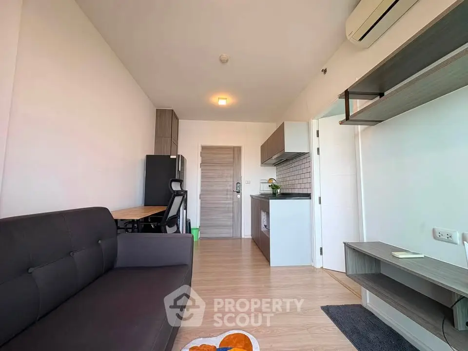 Modern apartment interior with open kitchen and cozy living area, featuring sleek furniture and wooden flooring.