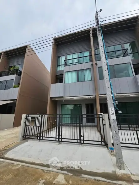 Modern three-story townhouse with sleek design and gated entrance in a suburban neighborhood.