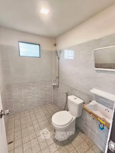 Spacious bathroom with modern fixtures and tiled walls, featuring a toilet and shower area.