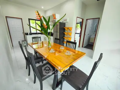 Modern dining area with elegant wooden table and black chairs in bright open kitchen layout.
