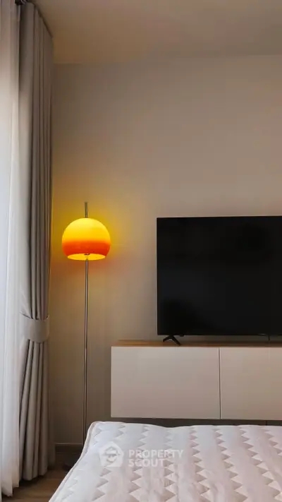 Modern bedroom with stylish lamp and wall-mounted TV, featuring elegant curtains and sleek furniture.