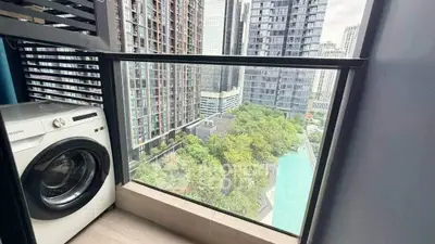 Modern high-rise balcony with washing machine and stunning city view overlooking pool and greenery.