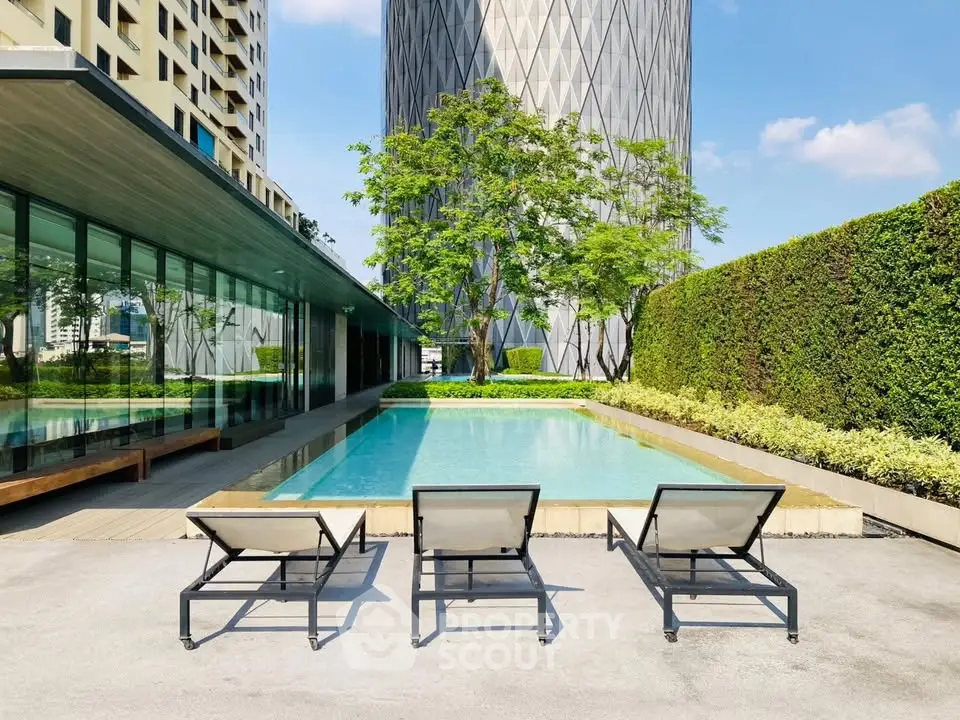 Luxurious modern apartment poolside with sleek lounge chairs and lush greenery, perfect for relaxation.