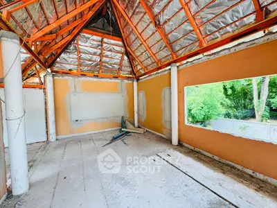 Spacious unfinished room with exposed beams and large window overlooking greenery.