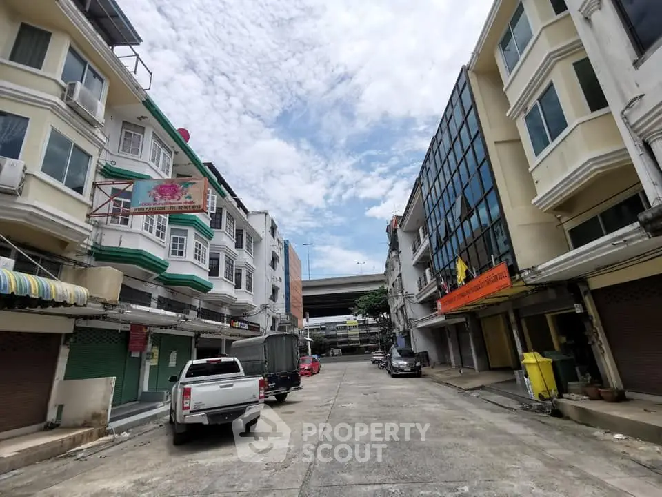 Charming urban street view with mixed-use buildings and parked vehicles under a bright blue sky.