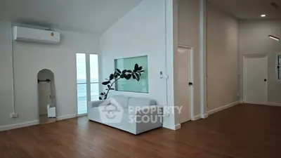 Spacious modern living room with sleek design and wooden flooring, featuring a cozy gray sofa and air conditioning.