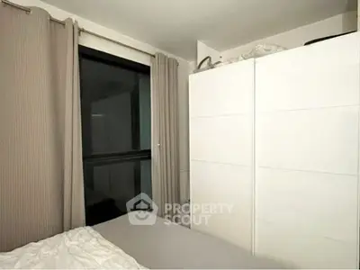 Cozy bedroom with modern wardrobe and large window, perfect for urban living.