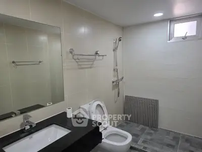 Modern bathroom with sleek fixtures and neutral tiles, featuring a shower and toilet.